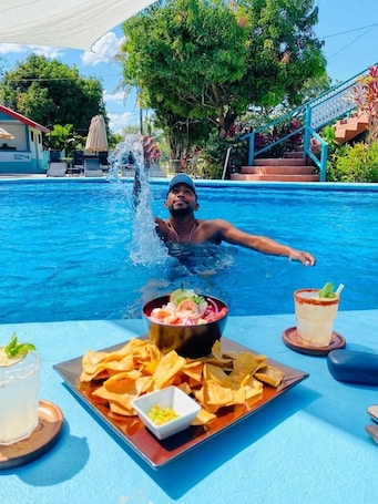 A poolside setting with a person in the water, a table with food and drinks, and a staircase in the background.. Drift Inn Cayo