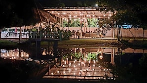 Un espacio al aire libre techado con mesas y sillas, rodeado de árboles y una masa de agua.