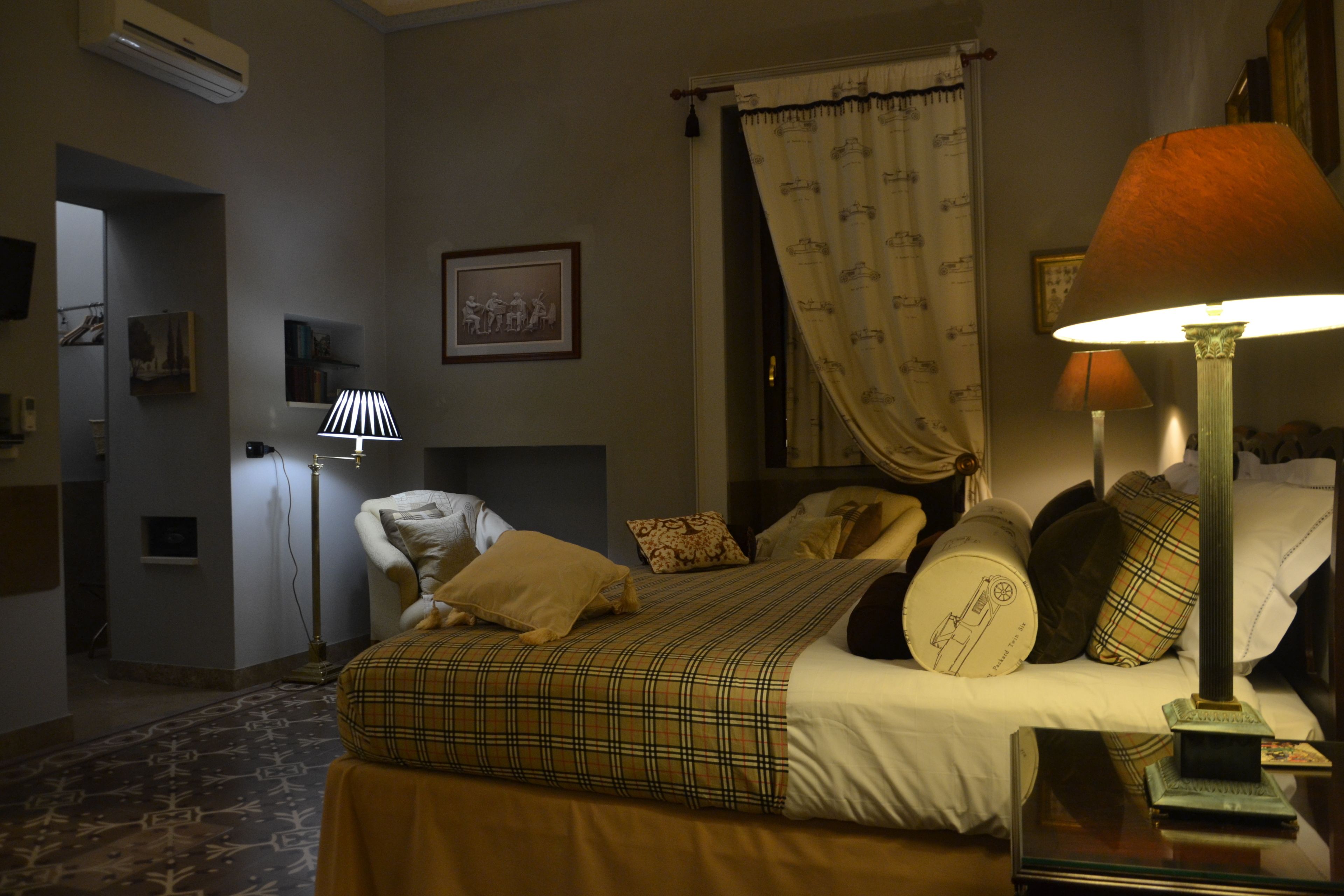 A hotel room with a bed, pillows, a lamp, a picture on the wall, and a curtain.