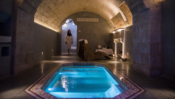 Ein Wellnessbereich mit einem Bogen aus Stein, einer Hot-Tub und einer Person im Bademantel.