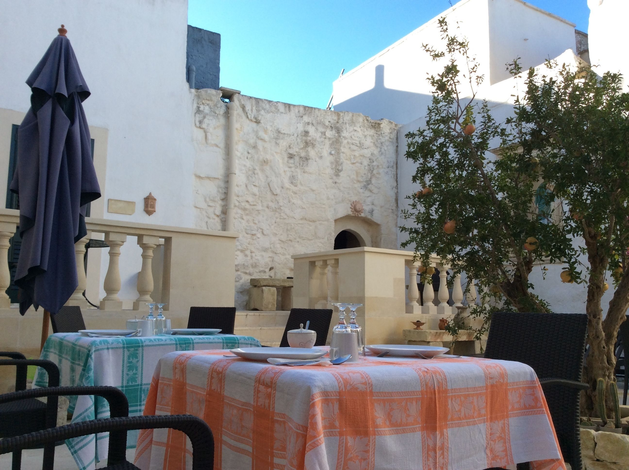 An outdoor dining area with tables set for two, covered with orange and white tablecloths.