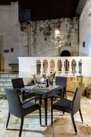 Un área de comedor al aire libre con sillas de mimbre y una mesa, frente a una pared de piedra con una lámpara colgante.
