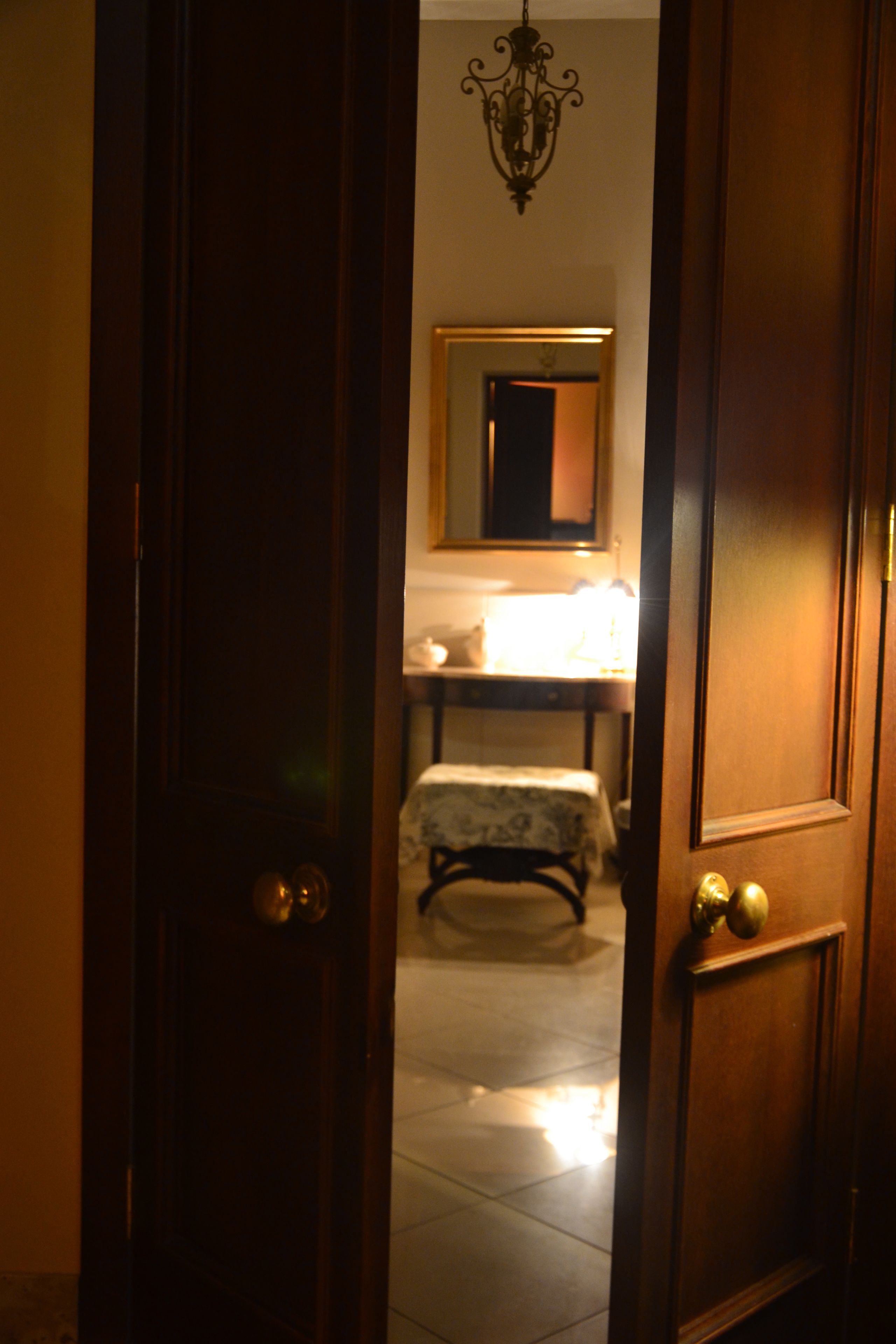 A wooden door leading to a room with a bed, a bedside table, and a mirror on the wall.