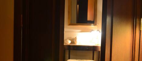 A wooden door leading to a room with a bed, a bedside table, and a mirror on the wall.