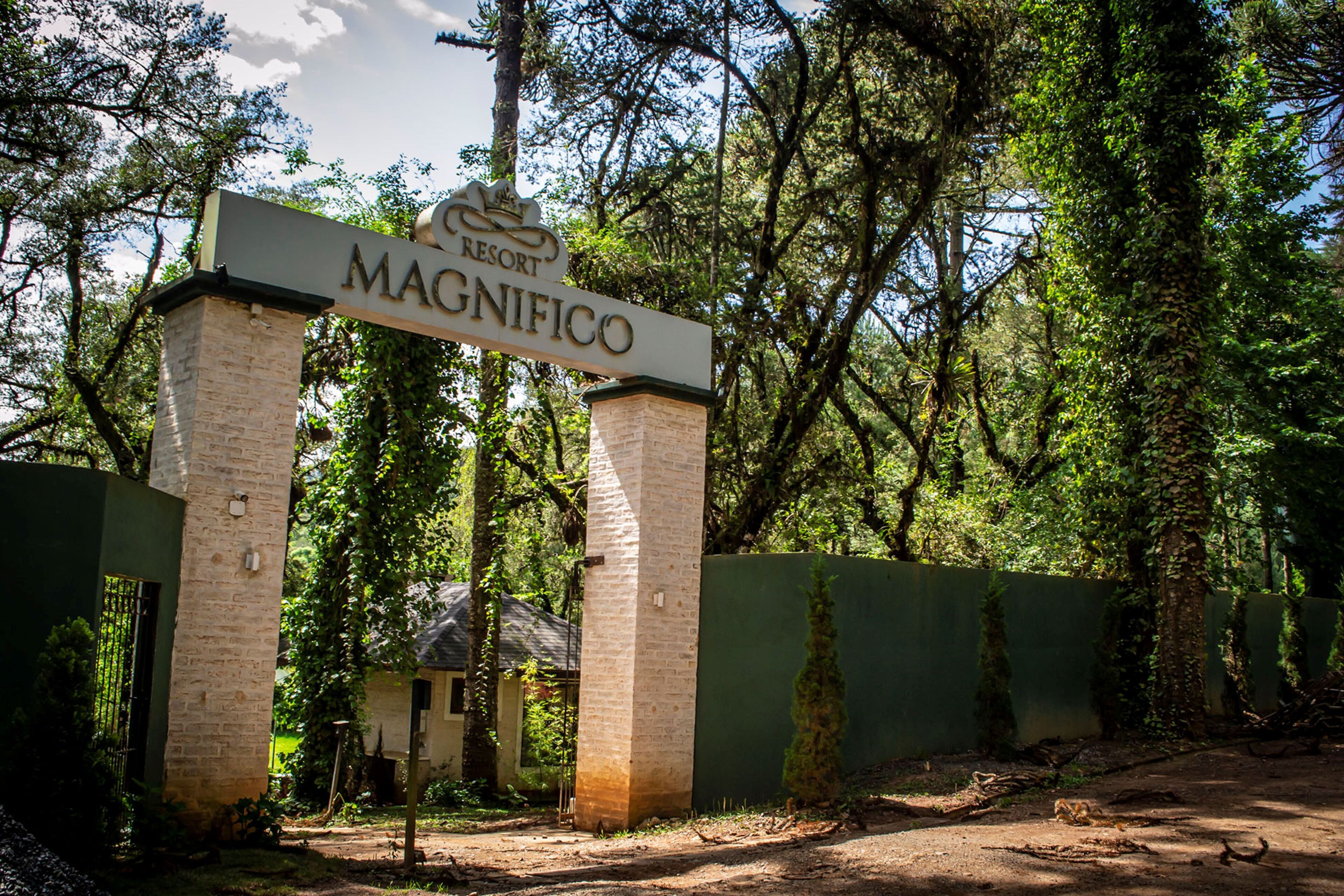 A sign for 'Resort Magnifico' with a brick pillar and a green fence in the background.