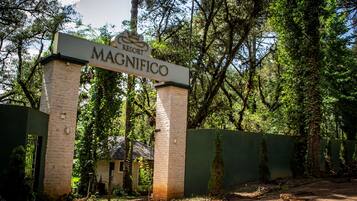 A sign for 'Resort Magnifico' with a brick pillar and a green fence in the background.