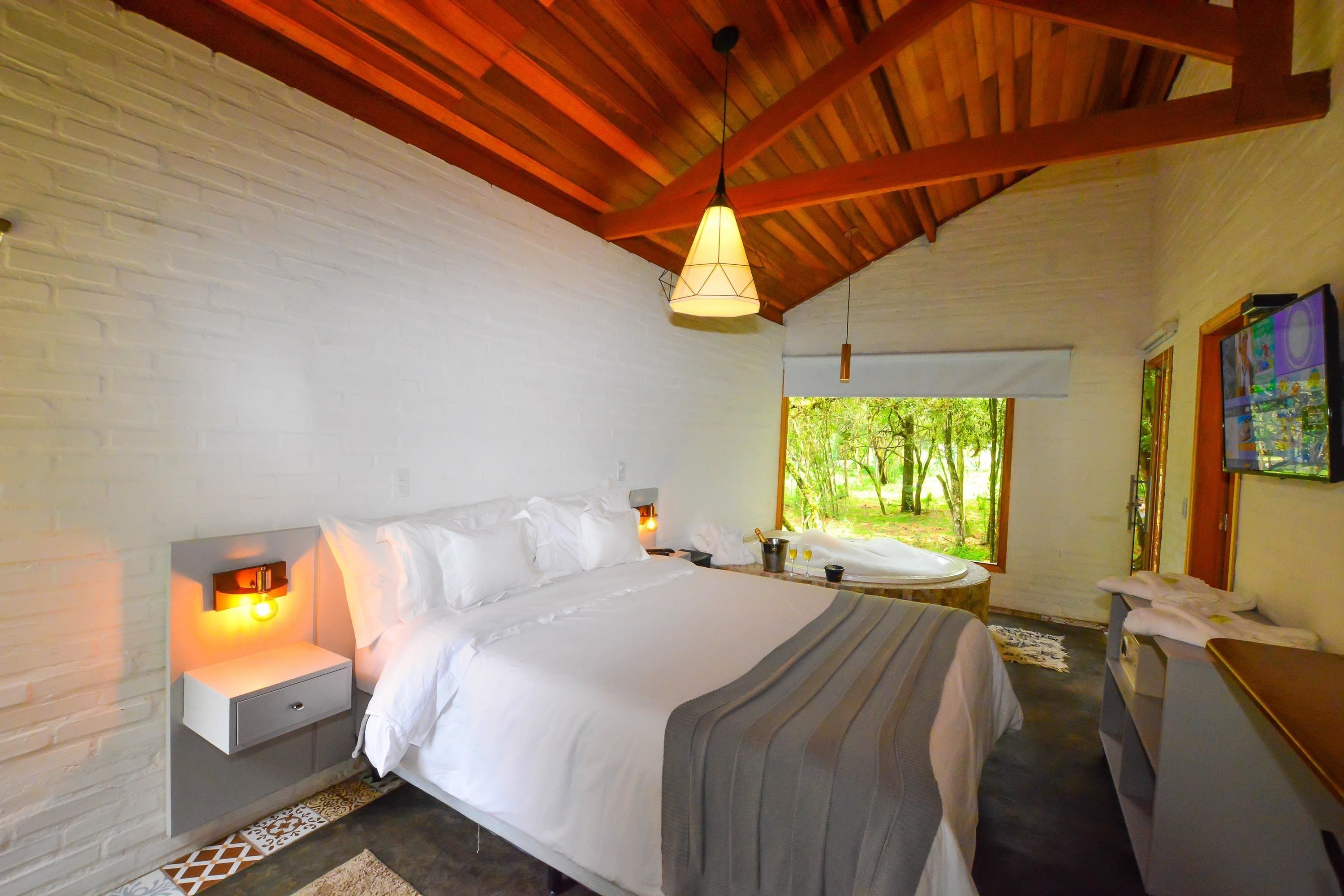 Un dormitorio con cama, mesitas de noche, un cabecero y una ventana con vistas a zonas verdes, además de techo de madera.