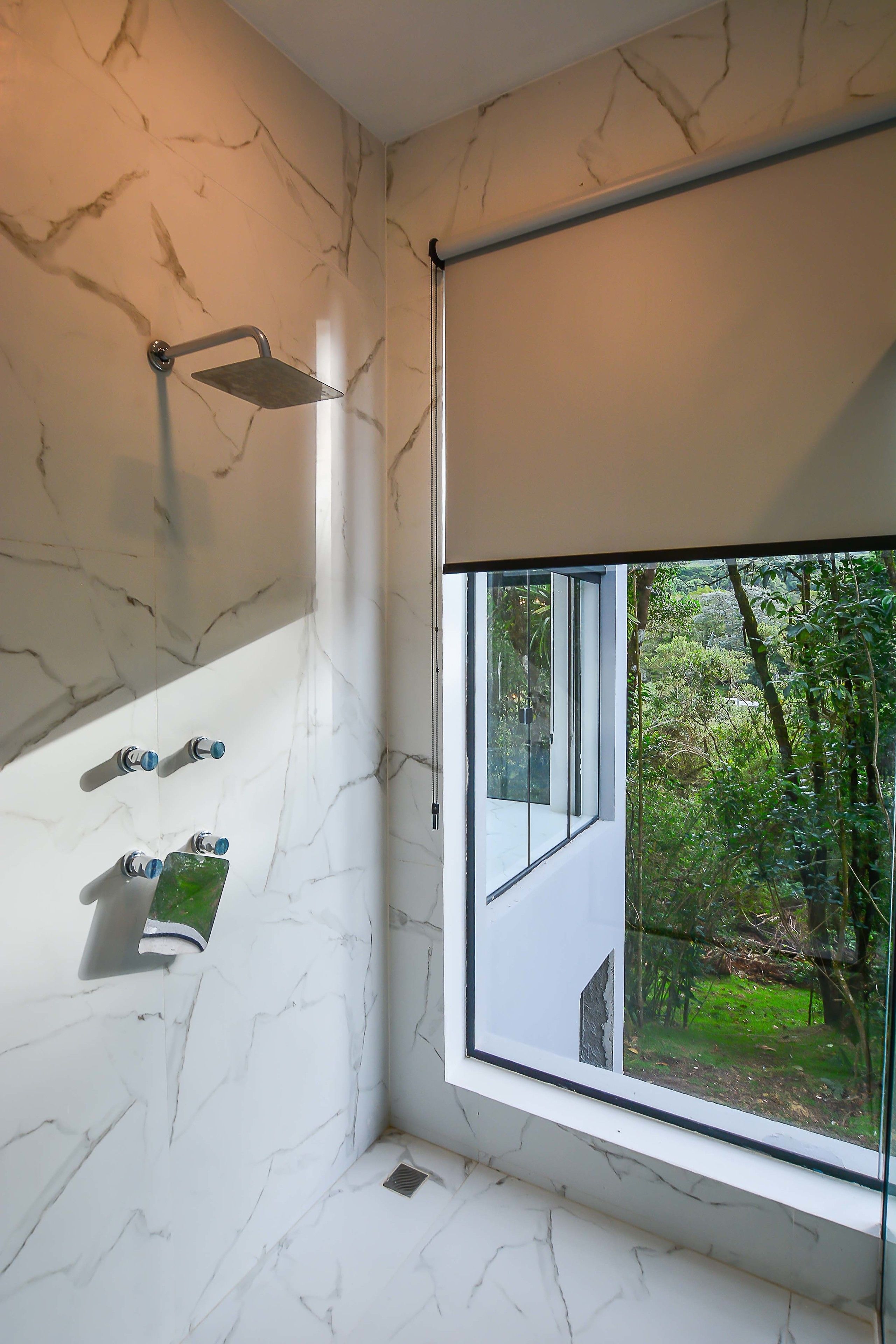 Une salle de bain avec un mur en marbre, une douche et une fenêtre donnant sur un paysage verdoyant.