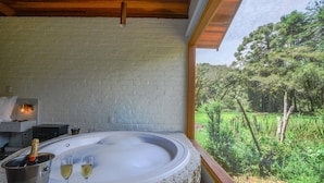 A hot tub with two glasses of wine and a bottle of champagne, surrounded by a white brick wall and wooden ceiling. - Resort Magnífico (Camanducaia)