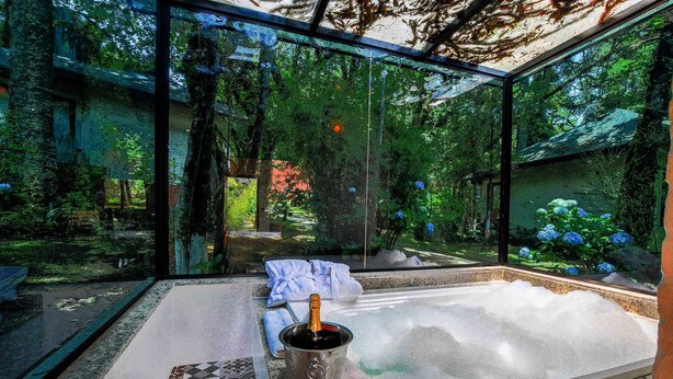 A glass-enclosed room with a hot tub, a bottle of champagne, and a glass. - Resort Magnífico (Camanducaia)