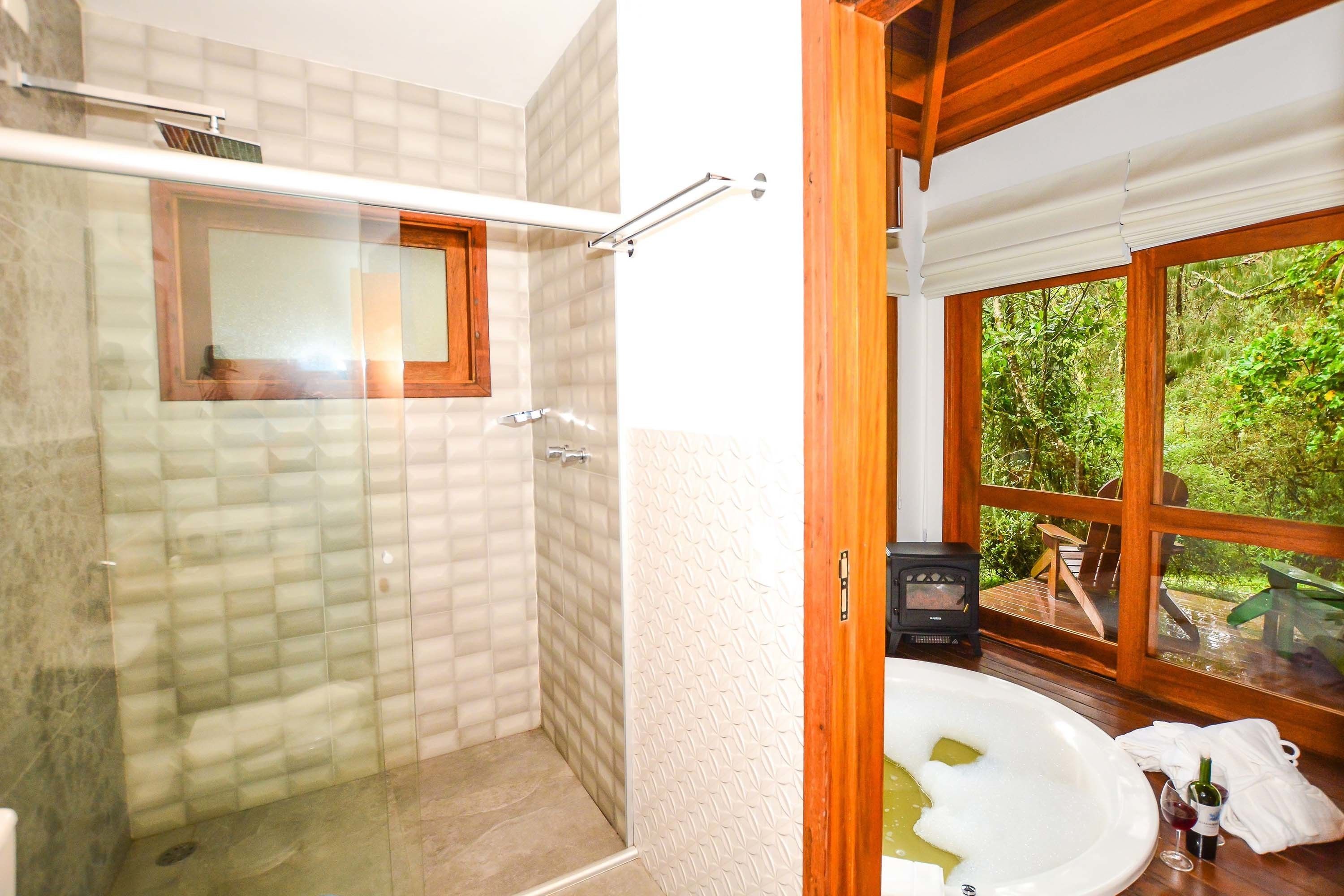 Een badkamer met een douchecabine van glas, een raam met houten kader en een bad vol schuim.