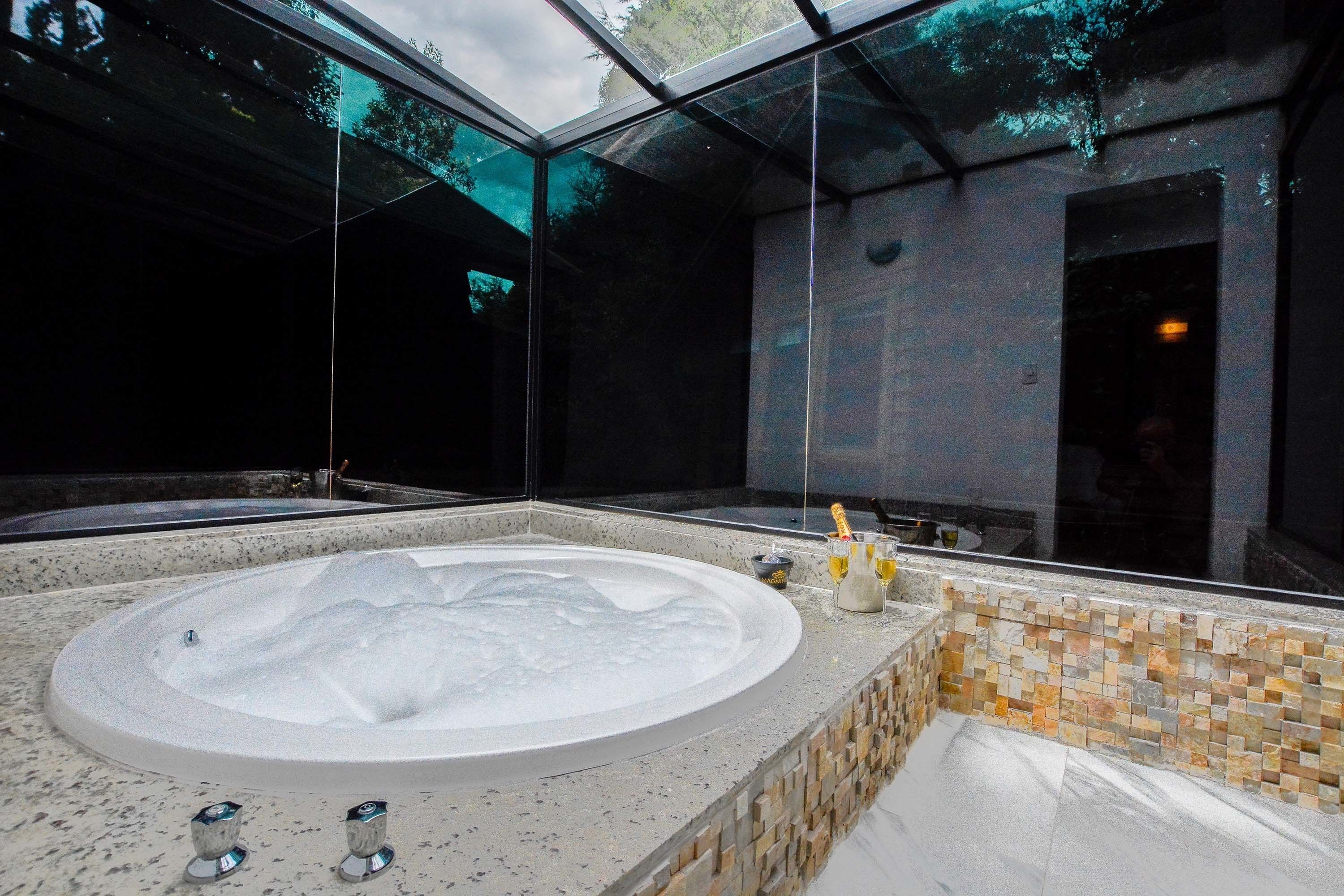 Un baño moderno con una bañera redonda independiente de gran tamaño, llena de hielo, una zona de ducha con cerramiento de vidrio y un muro cubierto de mosaicos.