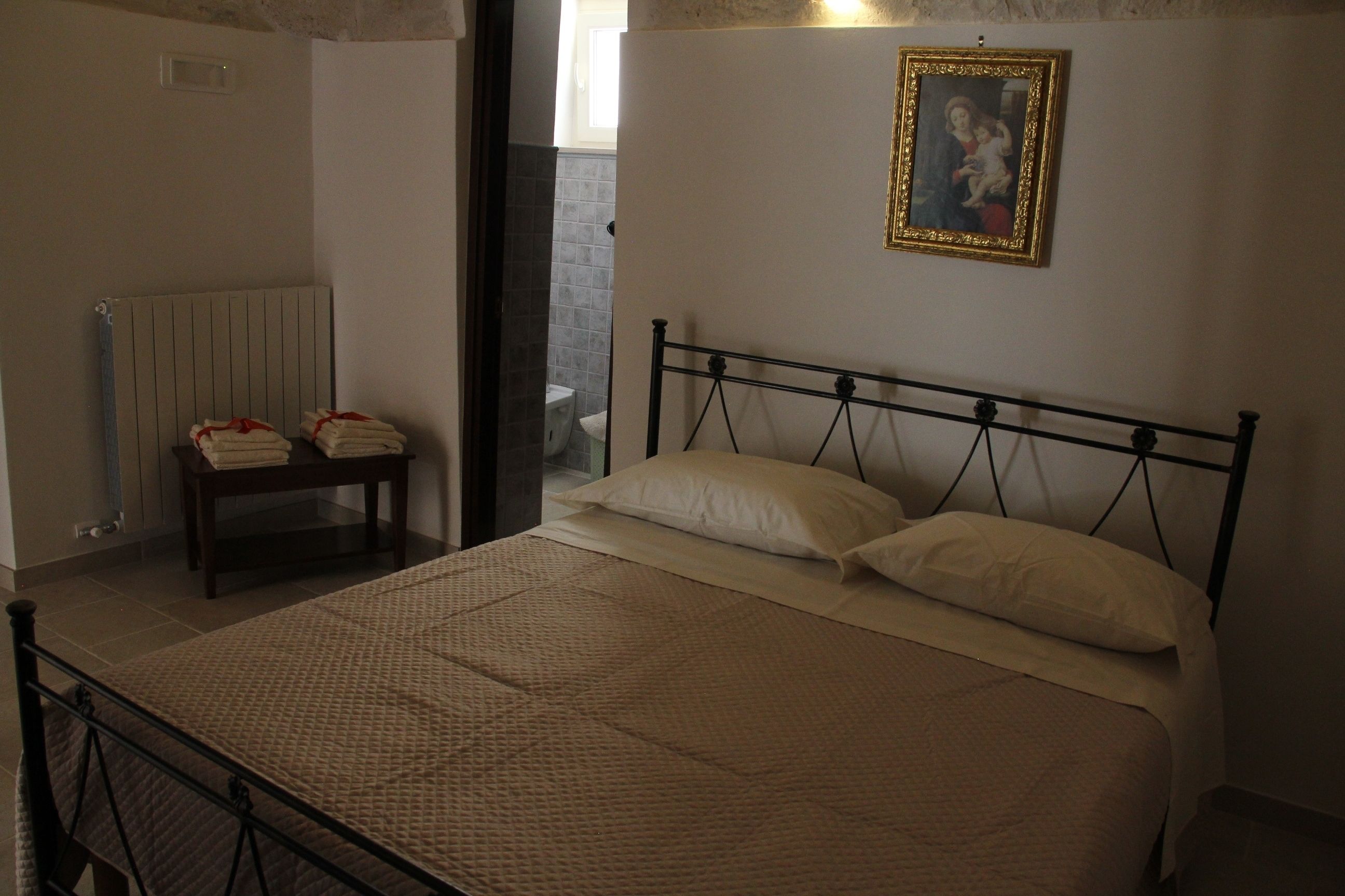 Une chambre à coucher avec un lit, une table de chevet avec des serviettes, un radiateur et un tableau encadré au mur.