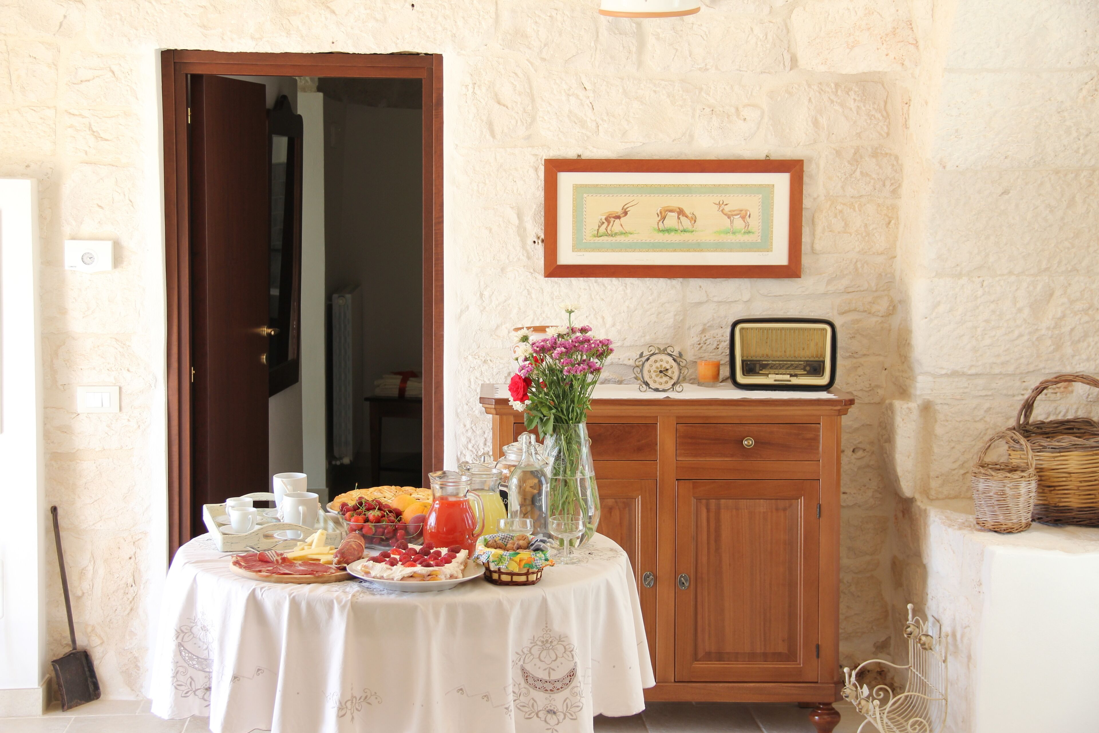 A breakfast table set with various food items and a vase of flowers, a wooden cabinet, and a framed picture on the wall.