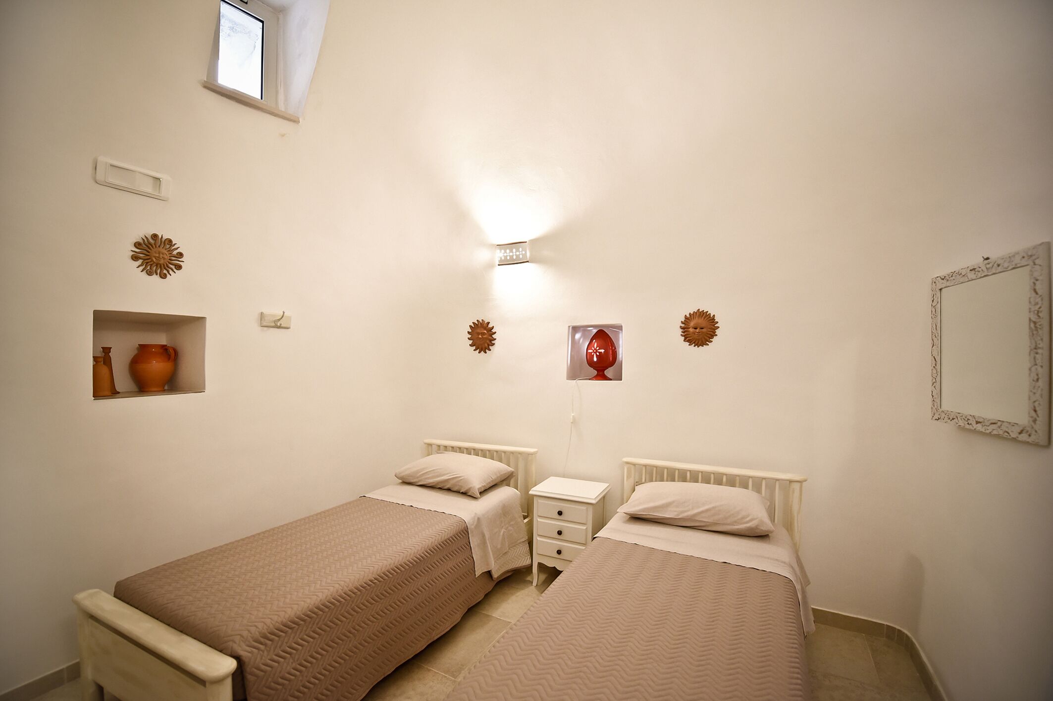 A bedroom with two beds, a small window, decorative wall art, and a mirror.