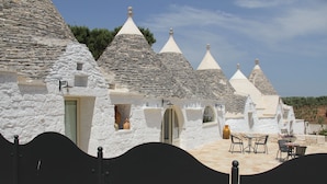 Una hilera de casas de piedra blanca con techos cónicos, un portón negro y mesas al aire libre.