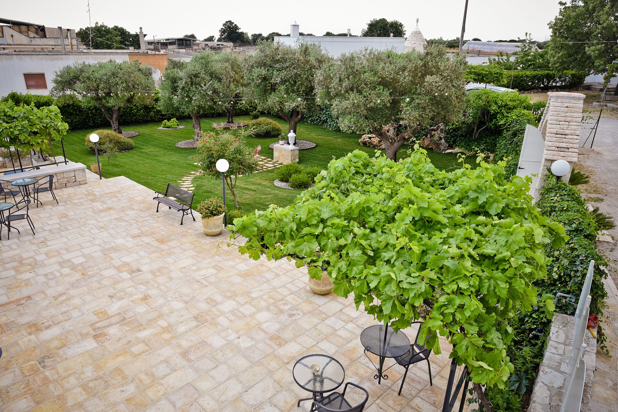 Un patio con suelo de piedra, mobiliario exterior y una variedad de plantas y árboles.