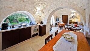Una cocina rústica con paredes de piedra, un ventanal grande y un comedor abierto con una mesa de madera.