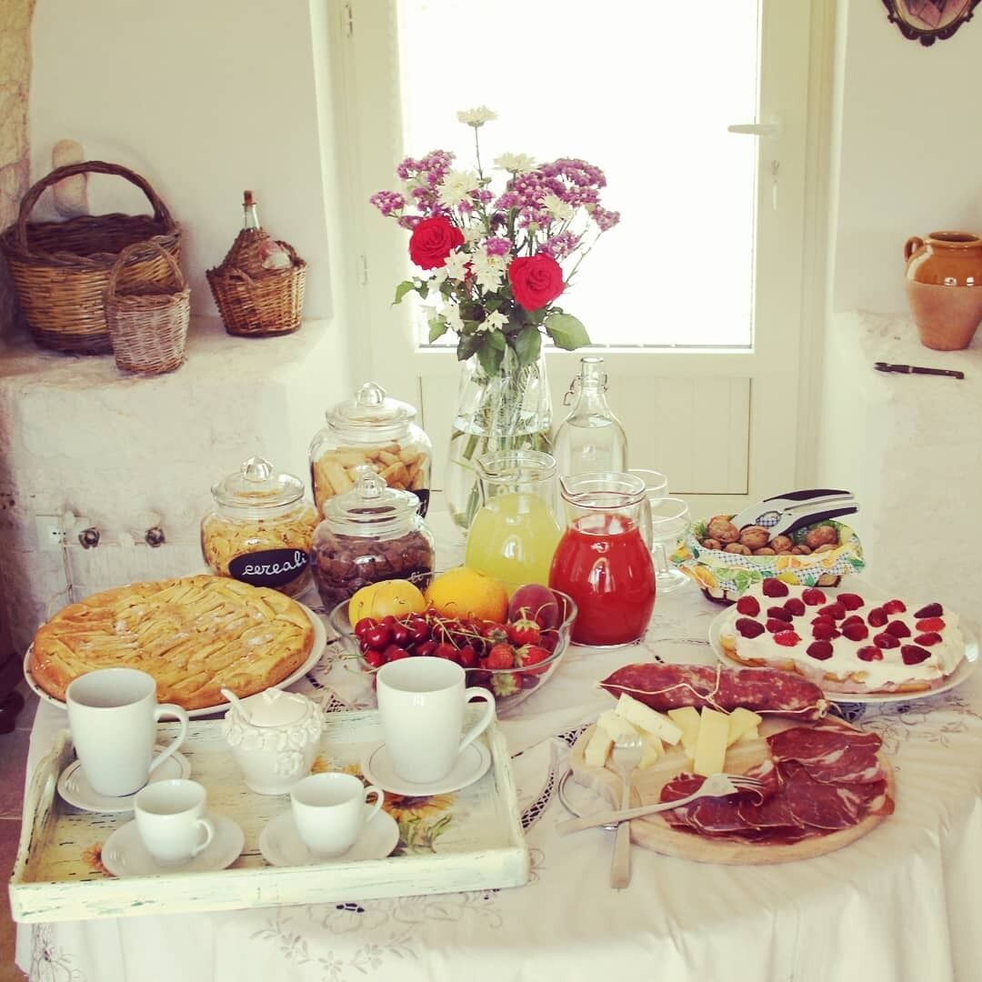 A breakfast spread with pastries, fruits, and beverages on a table near a window.