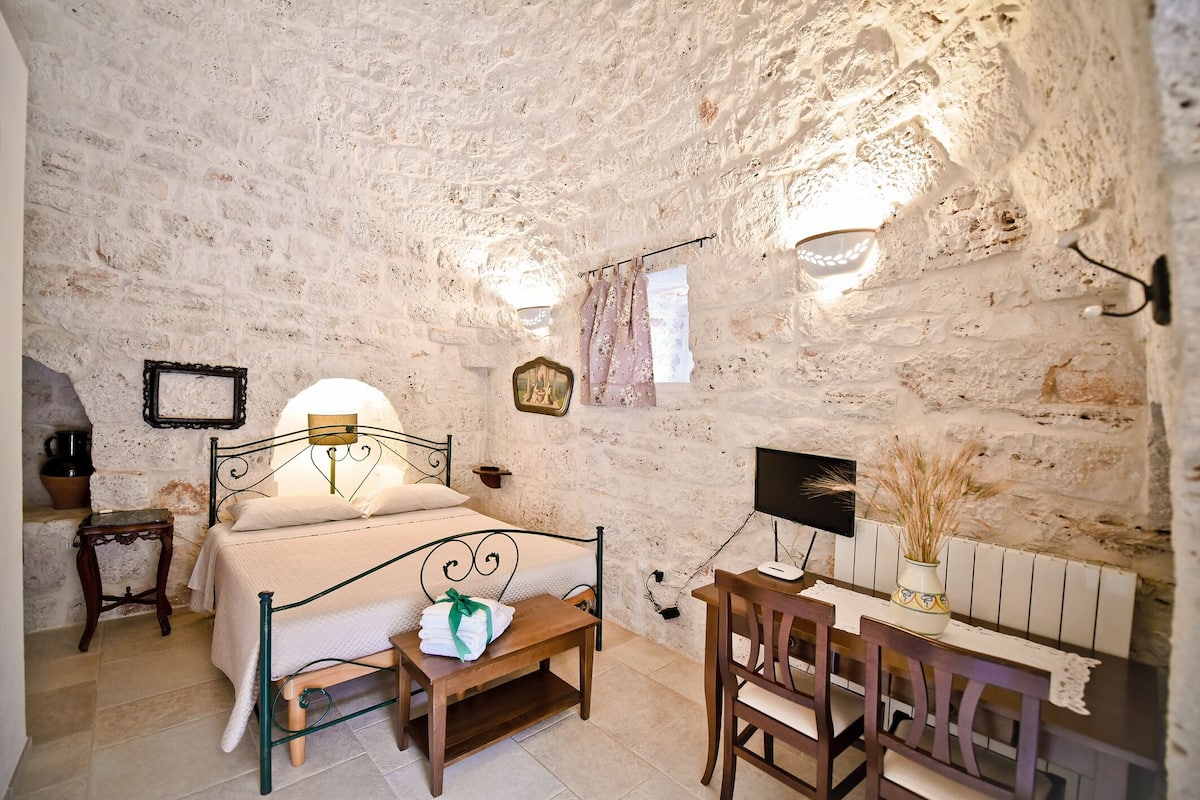 Un dormitorio rústico con pared de piedra, una cama, un escritorio y una silla.