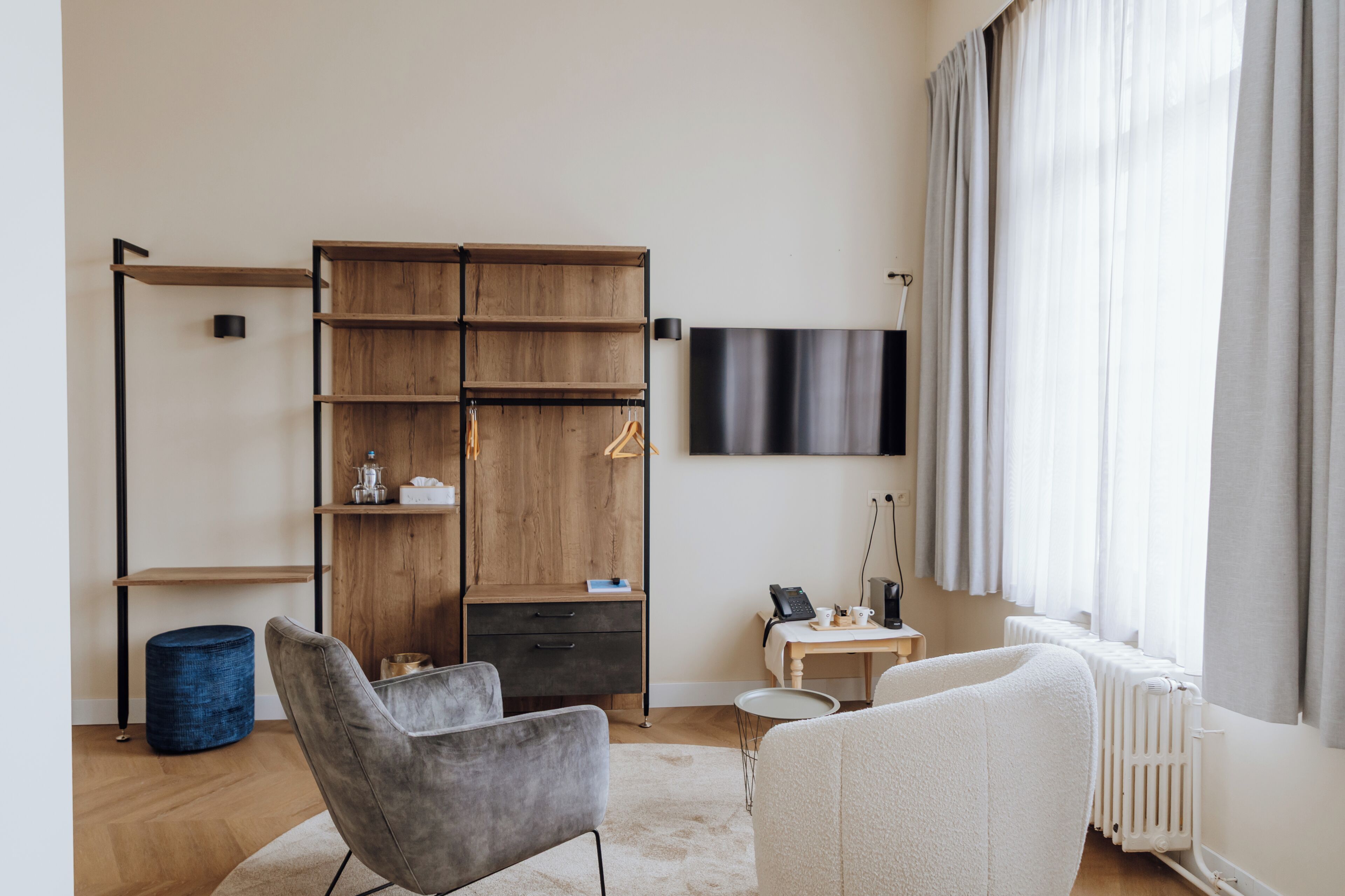 A modern room with a wooden bookshelf, a grey armchair, a white sofa, a small round table, and a mounted TV.