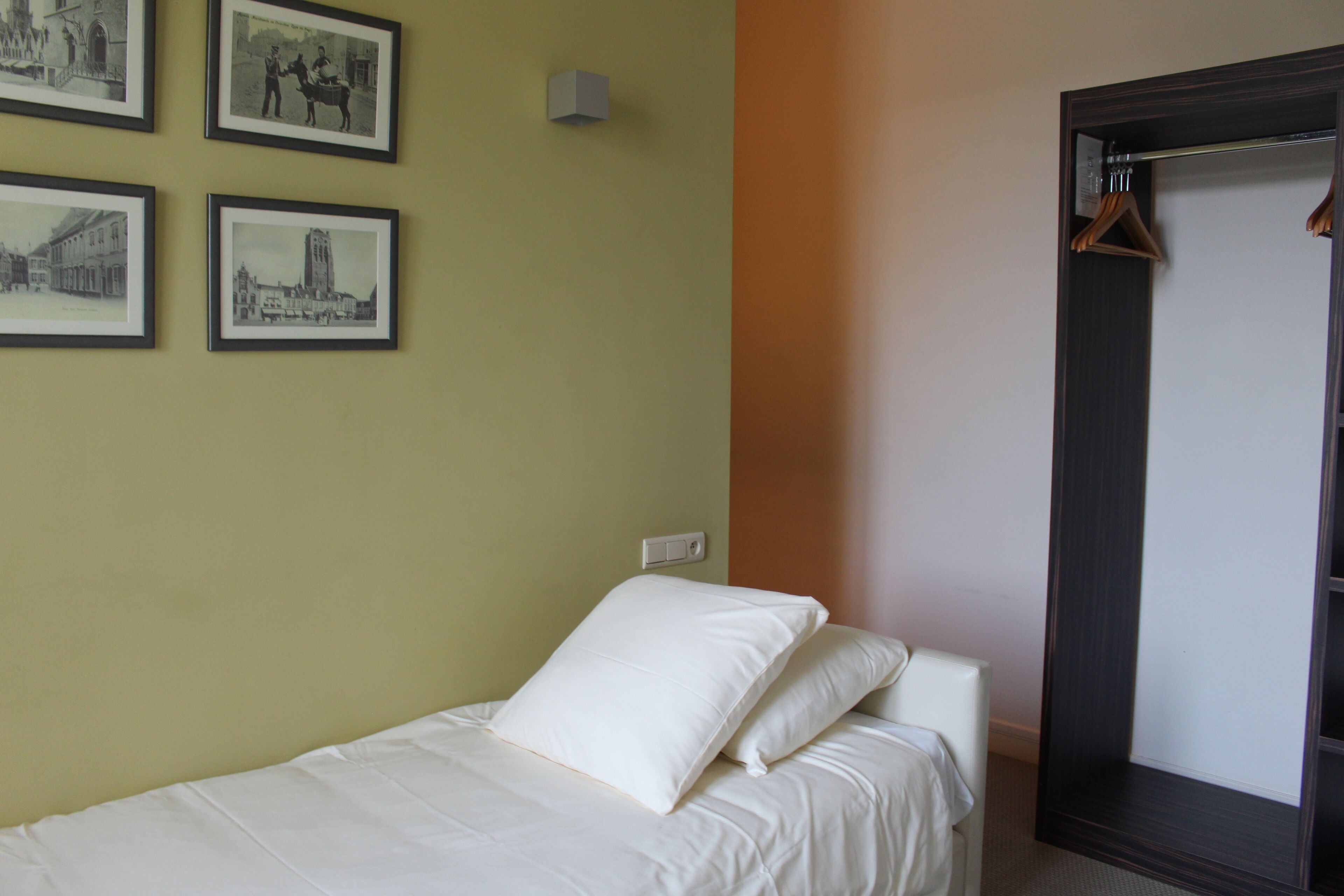 A hotel room with a bed, a wardrobe, and four framed pictures on the wall.