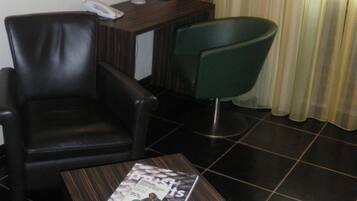 A hotel room with a leather chair, a small table with a magazine, a lamp, a phone, and a brick wall.