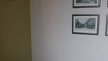 Un lit simple avec une literie blanche dans une pièce aux murs unis. Deux photographies en noir et blanc encadrées sont accrochées au mur.