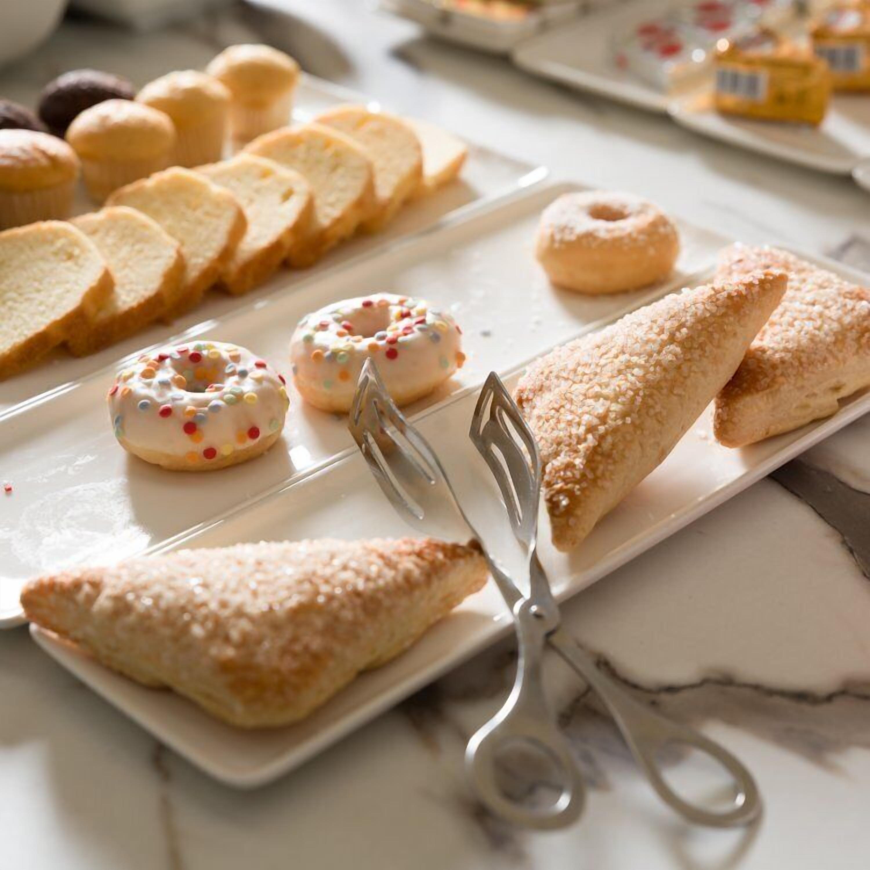 A variety of pastries and bread on a white plate with a pair of tongs.