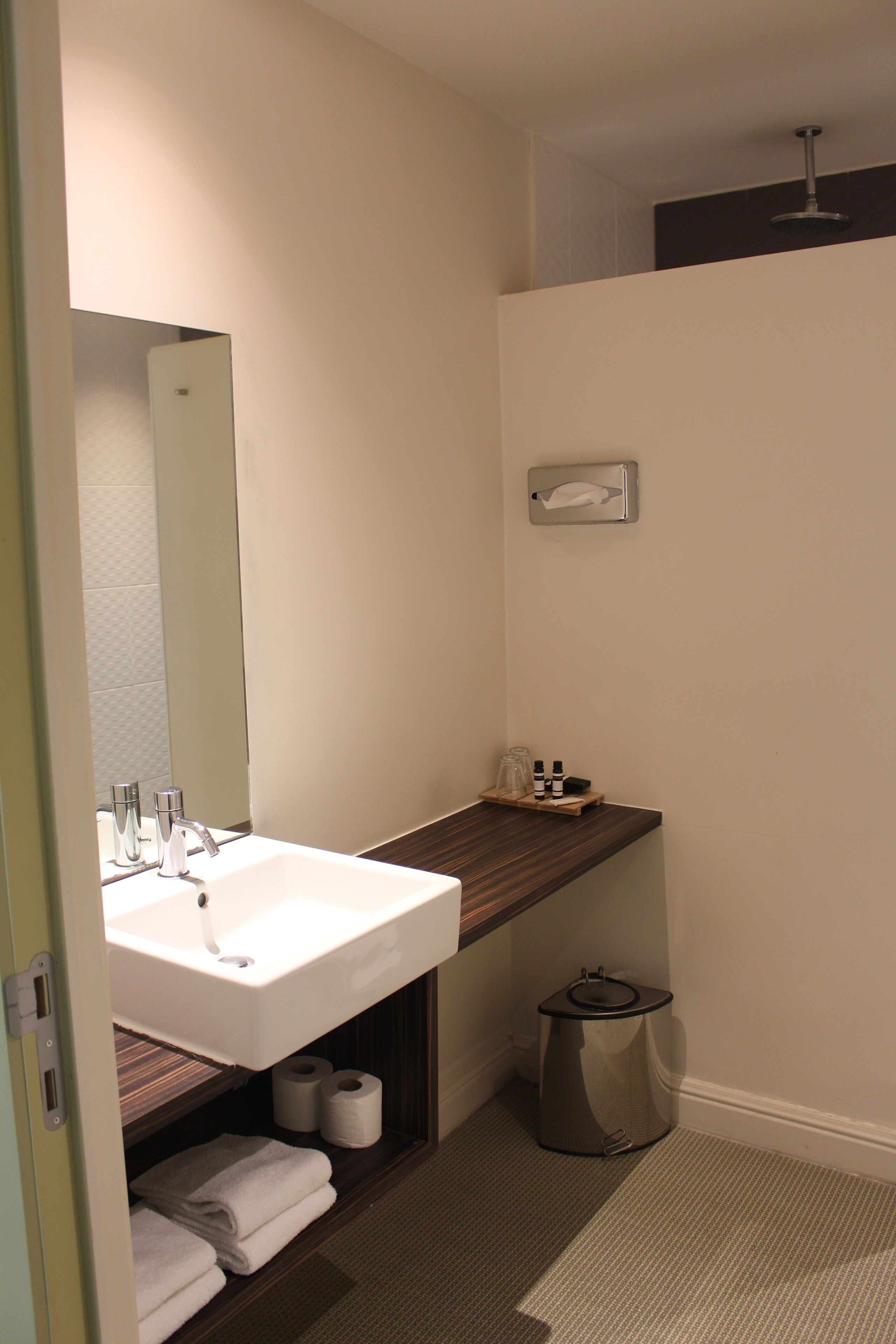 A bathroom with a white sink, mirror, and a small shelf with toiletries.