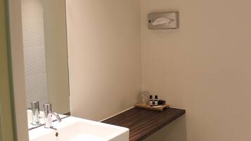 A bathroom with a white sink, mirror, and a small shelf with toiletries.