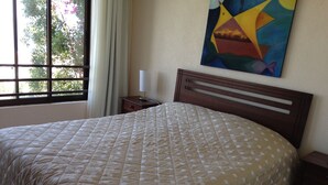 A neatly made bed with a quilted cover, a bedside table with a lamp, and a window with curtains. - Puerto Velero Andrea Meza 2 (Coquimbo)