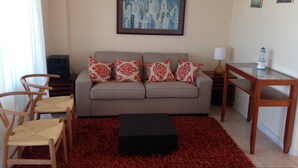 A living room with a sofa, two chairs, a coffee table, a lamp, and a painting on the wall. - Puerto Velero Andrea Meza 2 (Coquimbo)