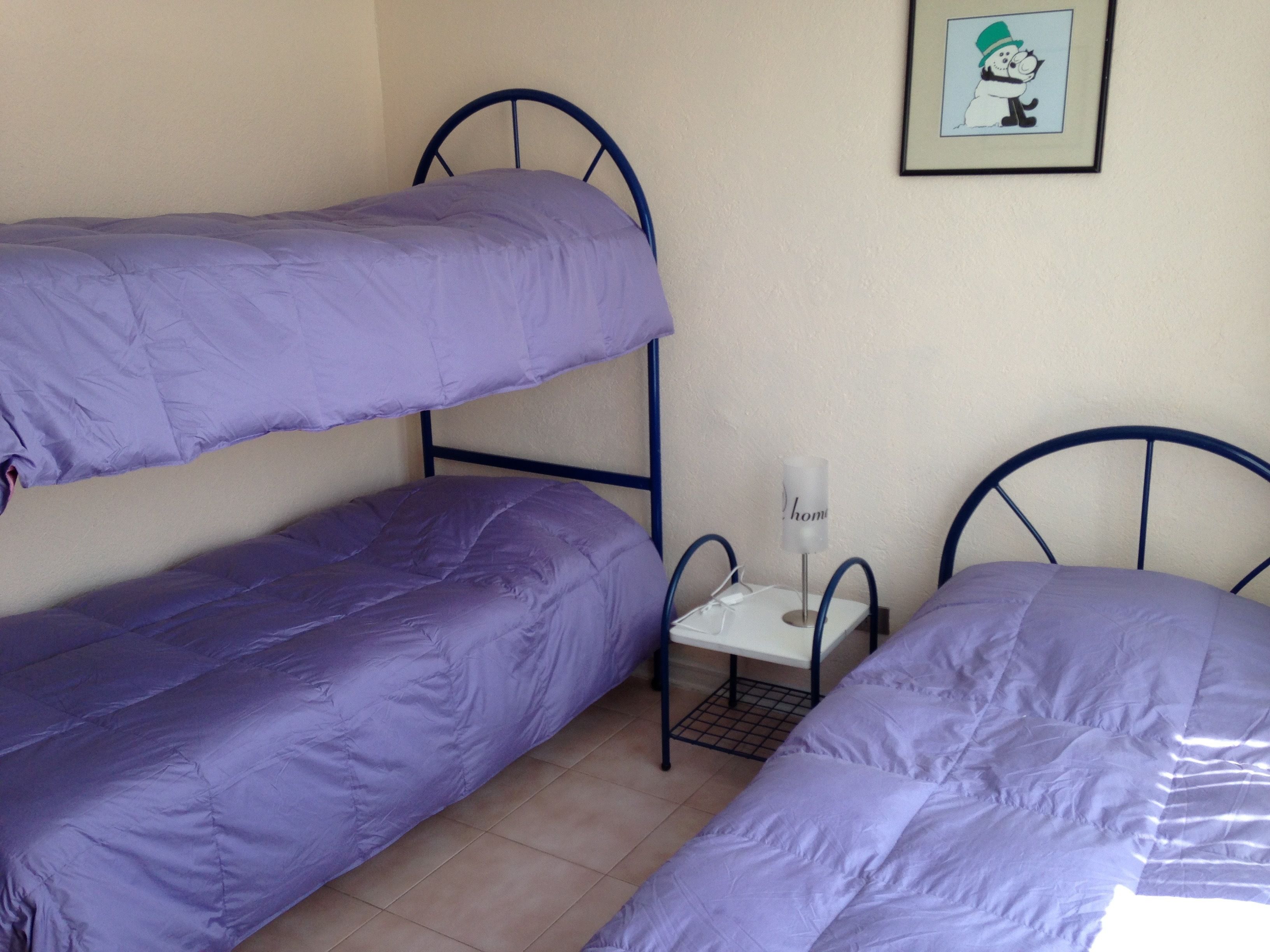 Un dormitorio con dos literas, una mesita con lámpara y un cuadro en la pared.