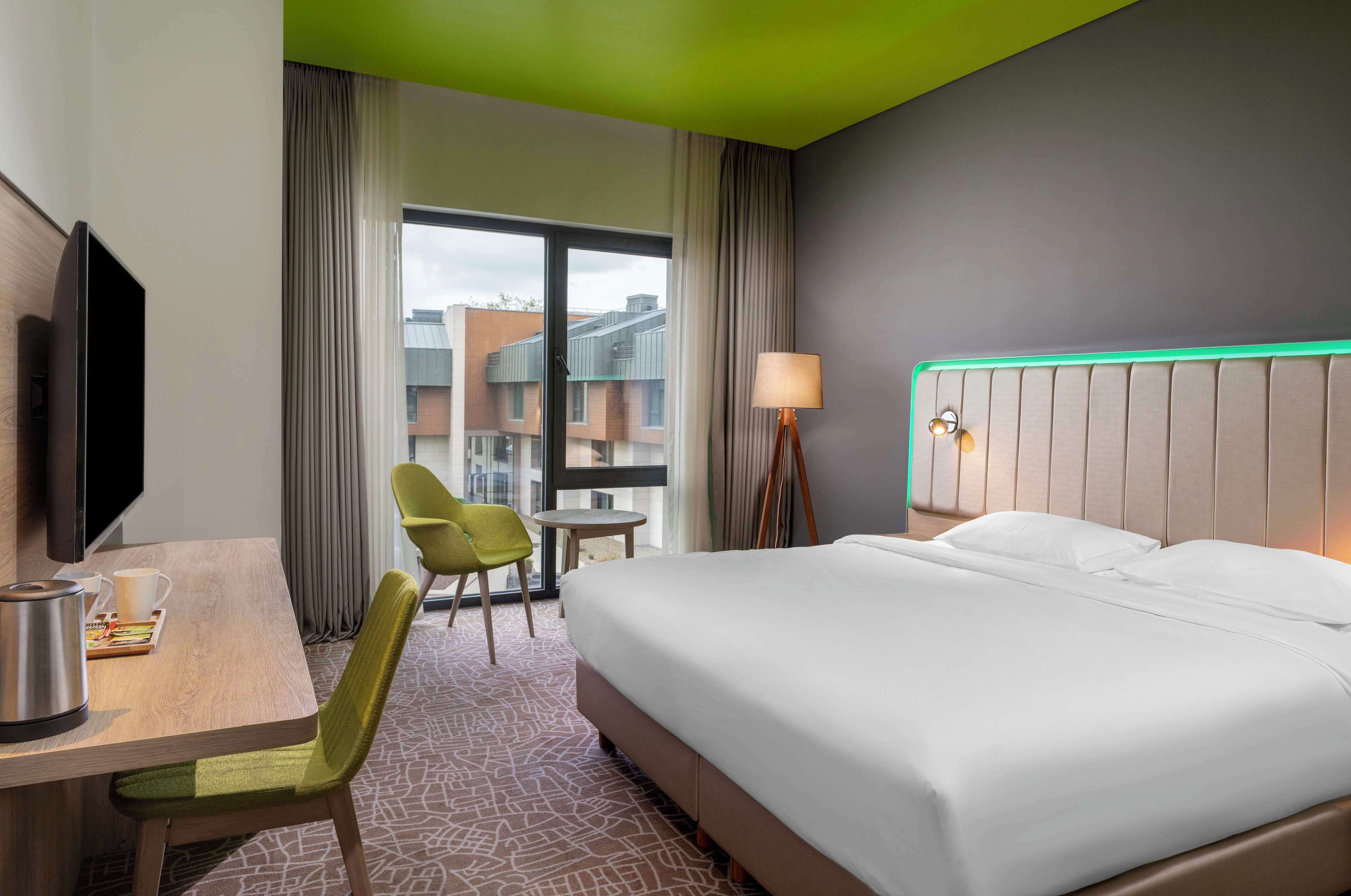 Una habitación de hotel con cama, escritorio, silla, televisor y lámpara.
