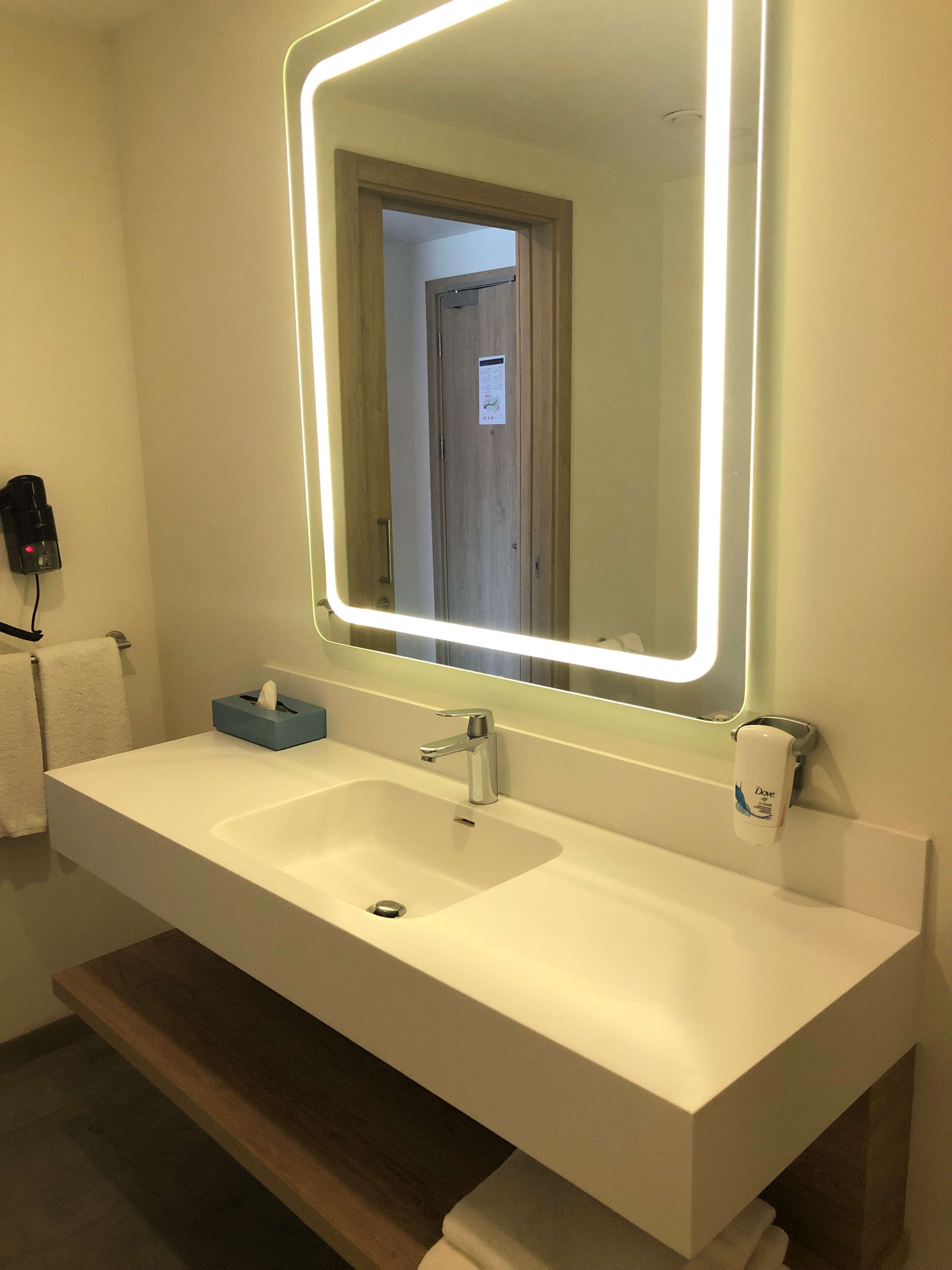 A bathroom with a white sink, a mirror with LED lights, a tissue box, and a hand soap dispenser.