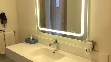 A bathroom with a white sink, a mirror with LED lights, a tissue box, and a hand soap dispenser.