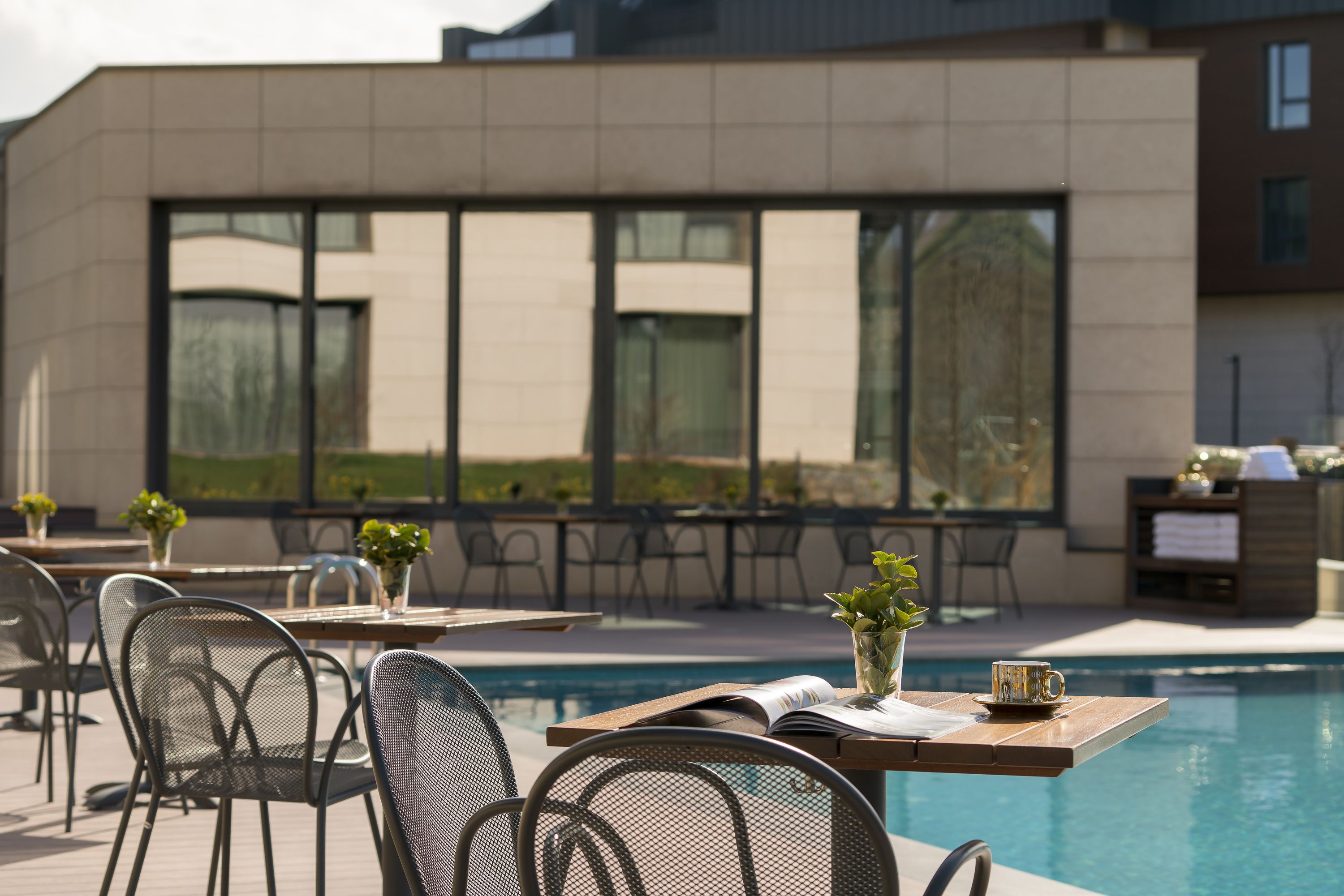 A poolside area with outdoor seating, a pool, and a modern building facade.