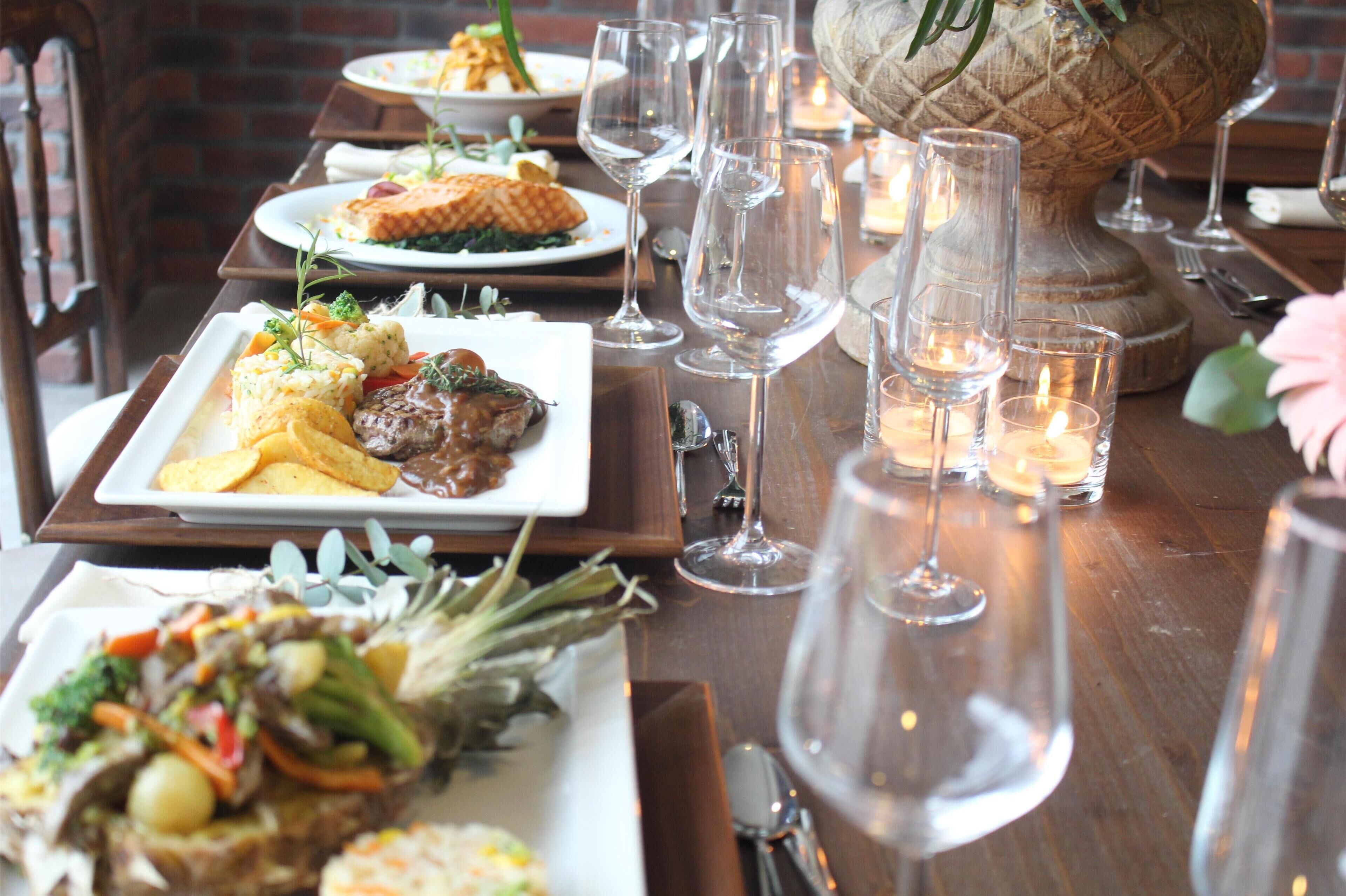 A dining table set with plates of food, wine glasses, and candles.