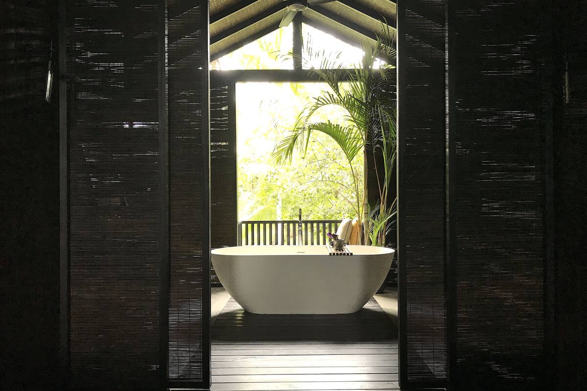 A large bathtub under a wooden structure with a view of greenery outside.