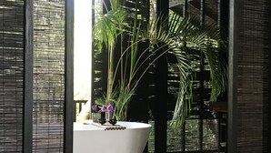 A modern bathroom with a white bathtub, a small sink, and a potted plant with purple flowers. - KAJU GREEN eco lodges (Unawatuna)