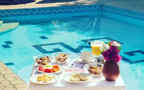 Disposição para o pequeno-almoço junto a uma piscina, com diversas opções de comida e bebida.