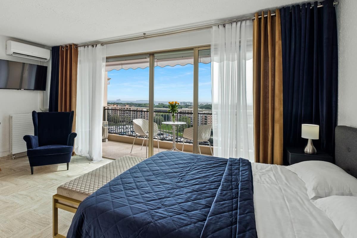 Habitación de hotel con cama, escritorio con silla, televisor montado en la pared y balcón con vista a la ciudad.