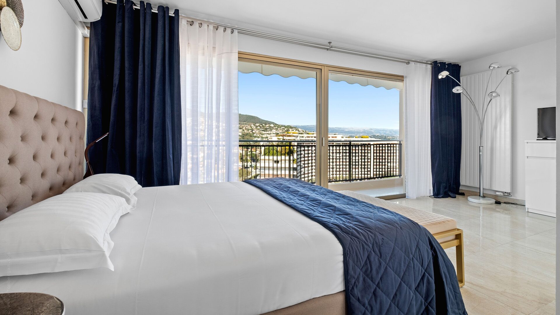 A bedroom with a large bed, a view of the city through a balcony, and a modern design.