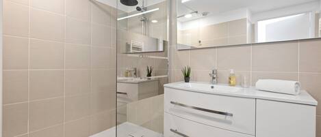 A modern bathroom with a glass shower enclosure, a white vanity with a mirror, and a sink.