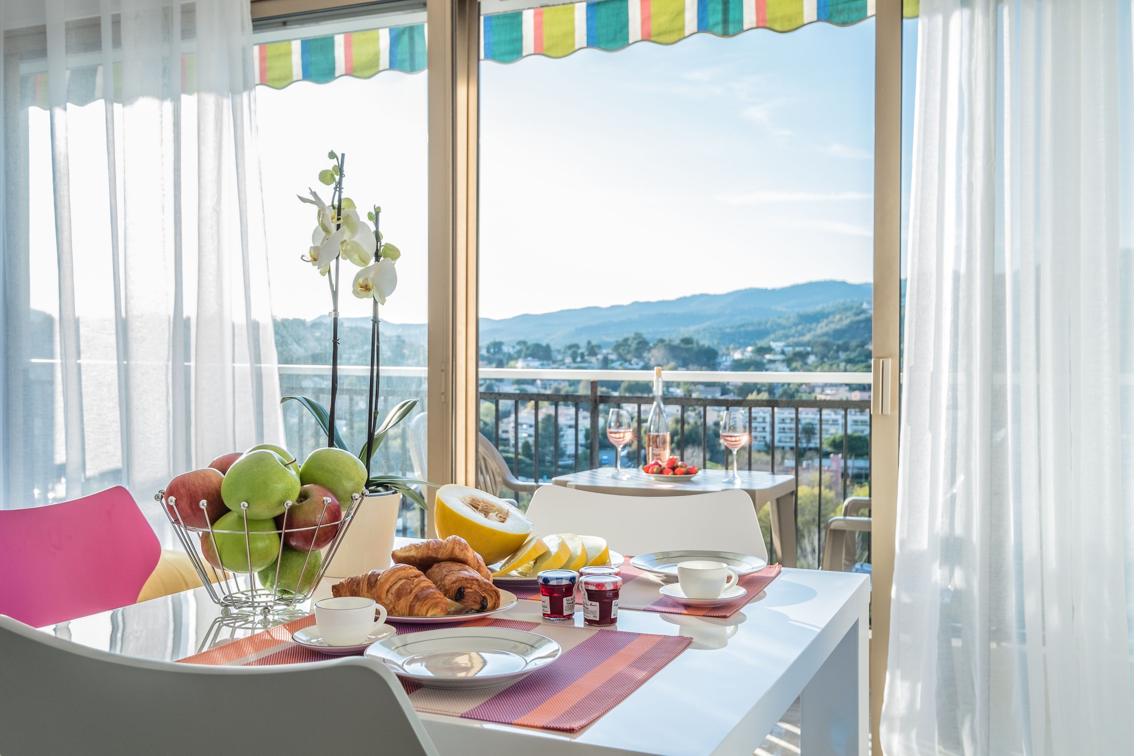 A breakfast table with fruits, pastries, and drinks, overlooking a scenic view.