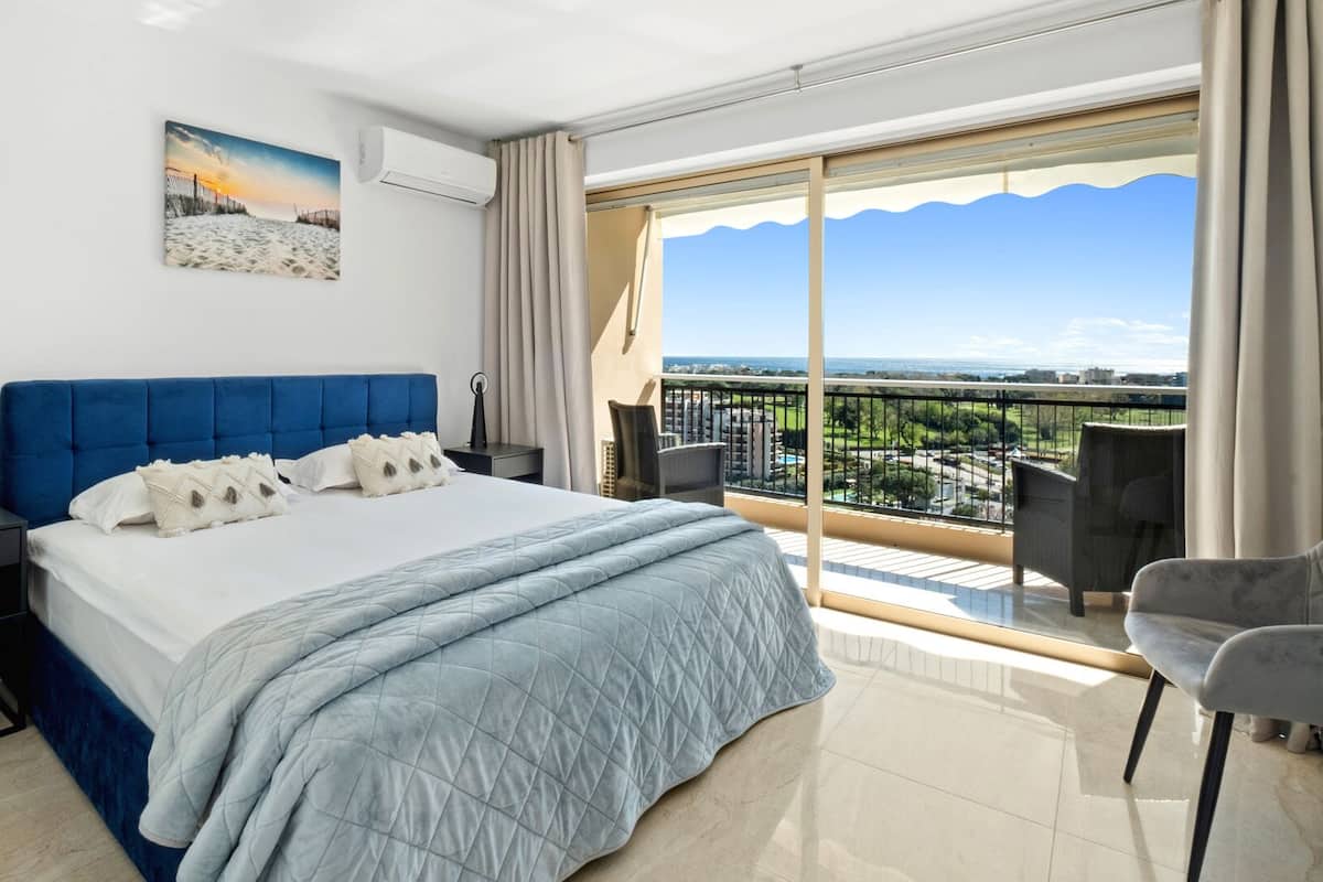 Una habitación de hotel moderna con una cama grande, un balcón con vistas y un cuadro en la pared.