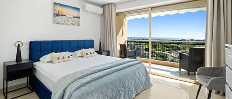 A modern hotel room with a large bed, a balcony with a view, and a painting on the wall.