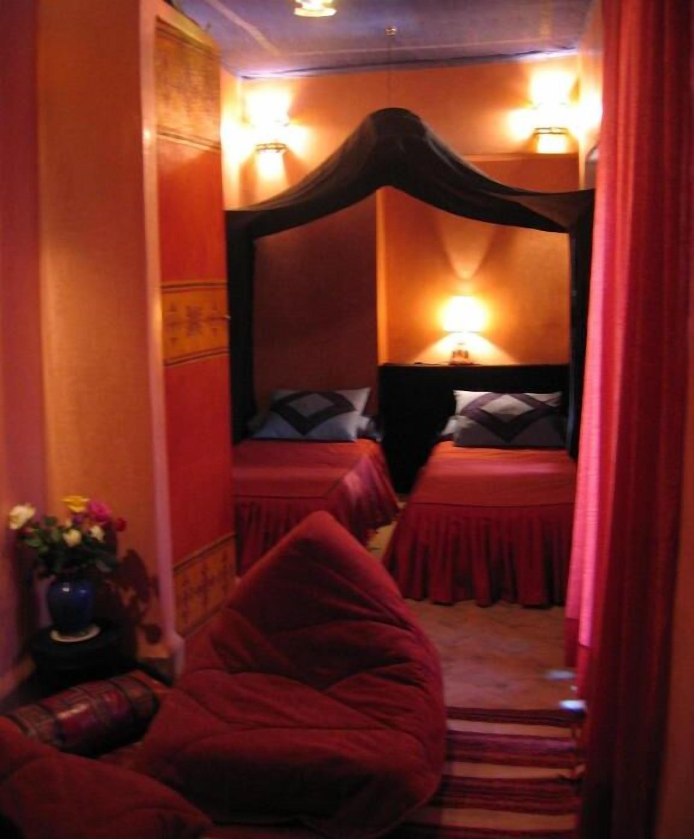 Une chambre avec un lit à baldaquin, deux tables de chevet, une petite chaise et un vase rempli de fleurs.