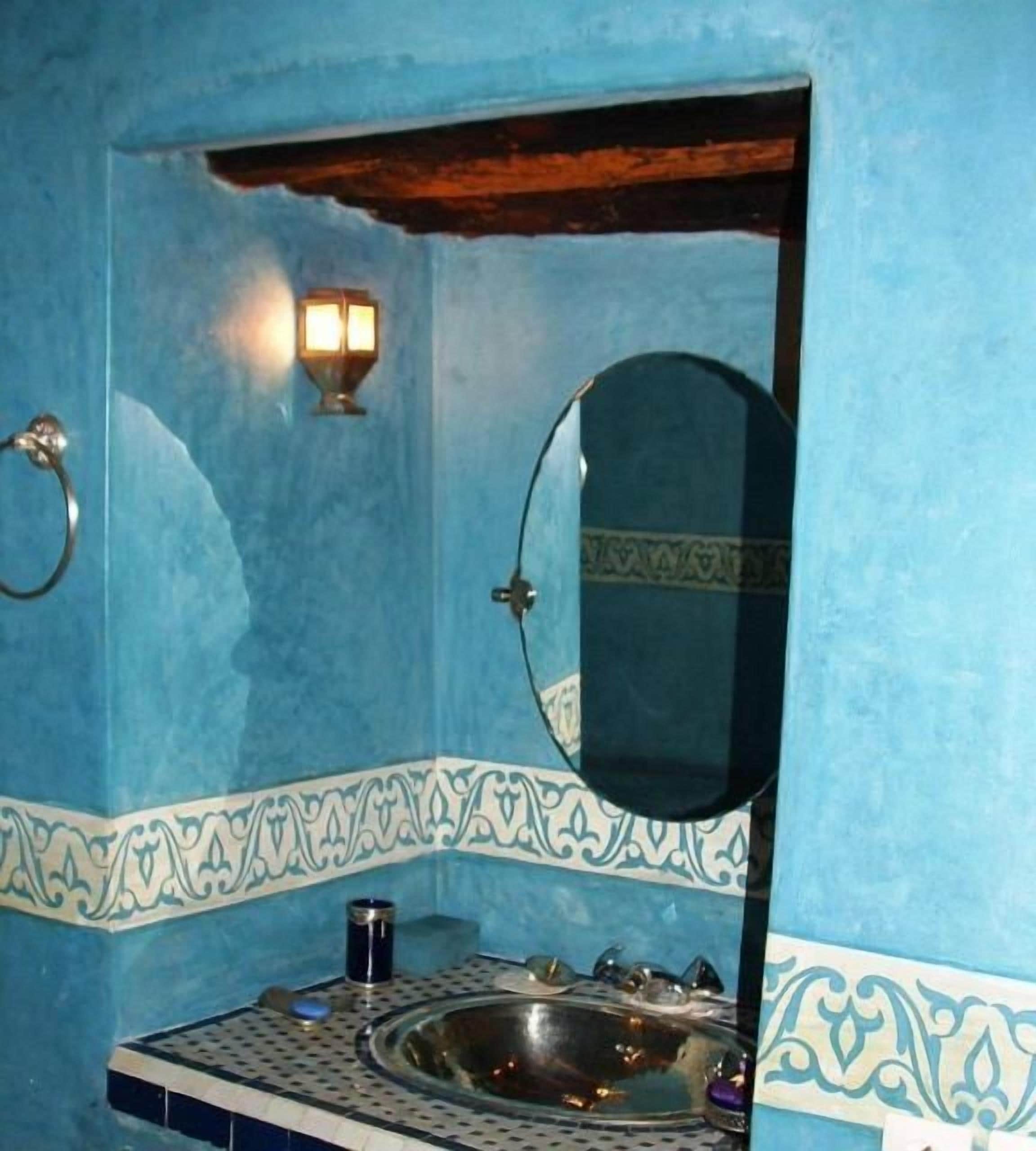 A bathroom with a blue tiled wall, a sink with a mirror, and a wall-mounted light fixture.